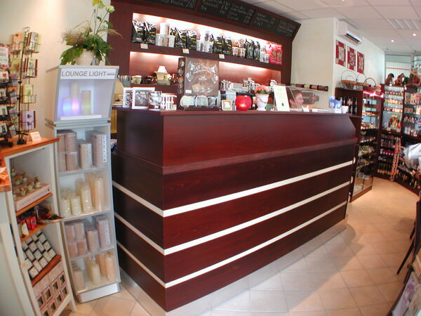 Gemütlicher Verkaufsraum mit Holztresen, Regalen voller Feinkost, Kerzen und Geschenkartikeln.