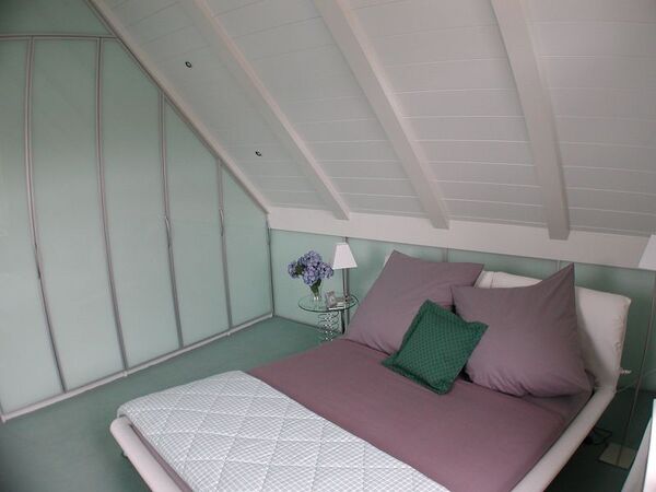 Gemütliches Schlafzimmer im Dachgeschoss mit modernem Bett, Glasfront und Dekokissen.