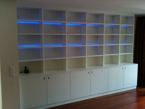 Modernes weißes Regal mit LED-Beleuchtung und Schranktüren im Wohnzimmer auf Parkettboden.
