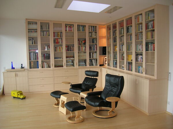 Helles Wohnzimmer mit großer Bücherwand, Ledersesseln und modernem Holzregal.